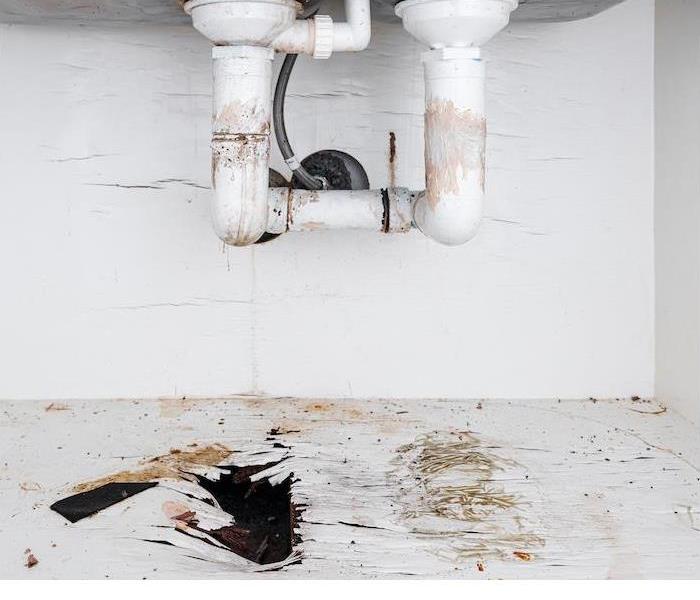 The underside of a sink showing water damage from leaking pipes